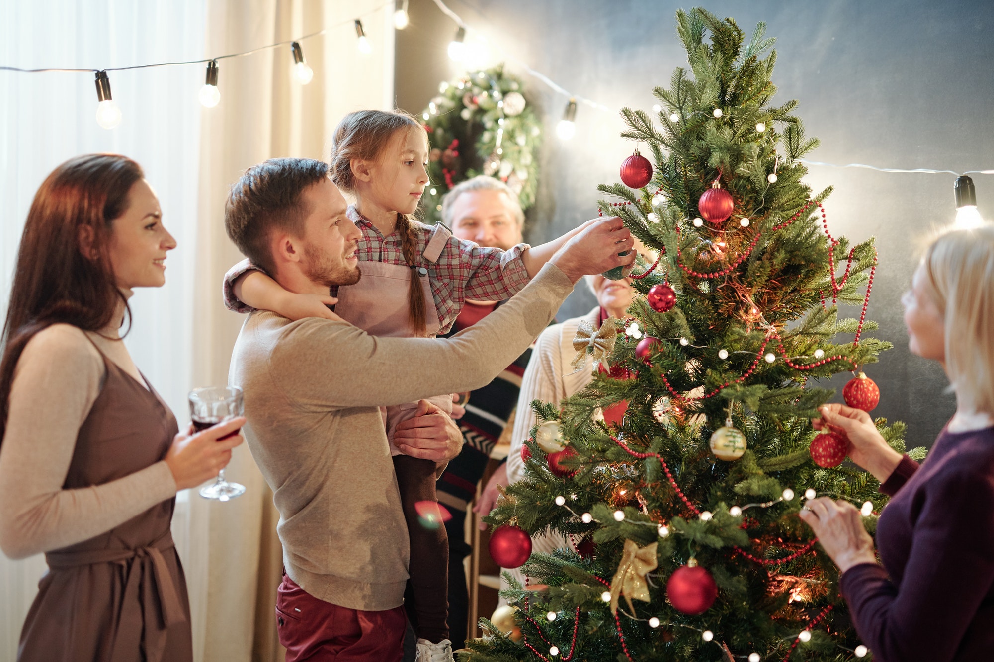 Young man with his little daughter decorating Christmas tree at home
